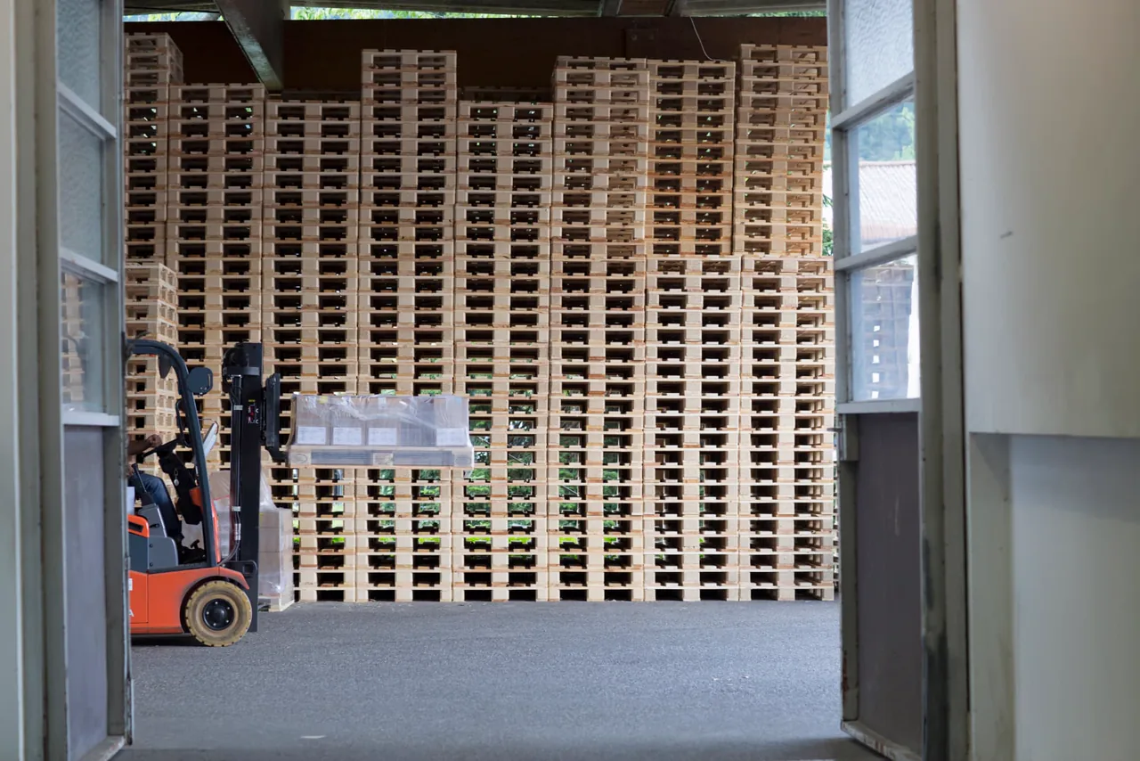 Stacked wooden pallets and a forklift inside a working warehouse